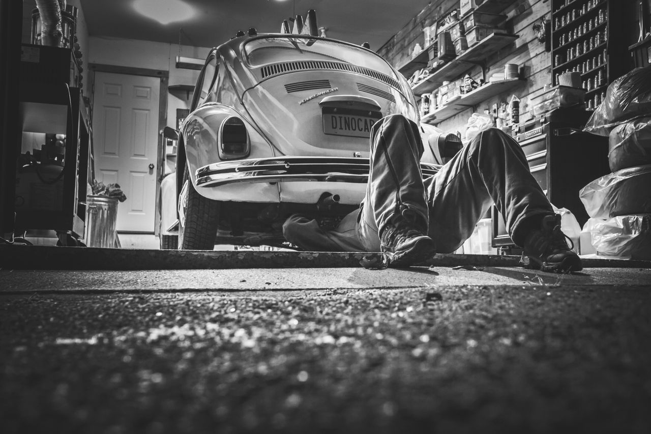 core-values Mechanic working beneath a classic Volkswagen Beetle in a vintage garage setting.