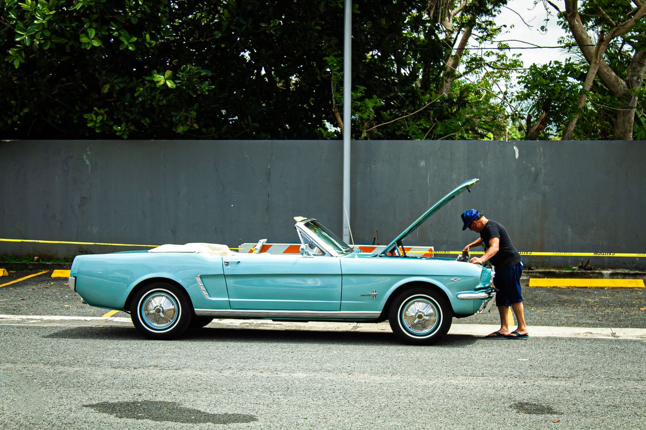 creative-approach-img A man checks a vintage blue convertible parked on a street, displaying a classic, nostalgic scene outdoors.