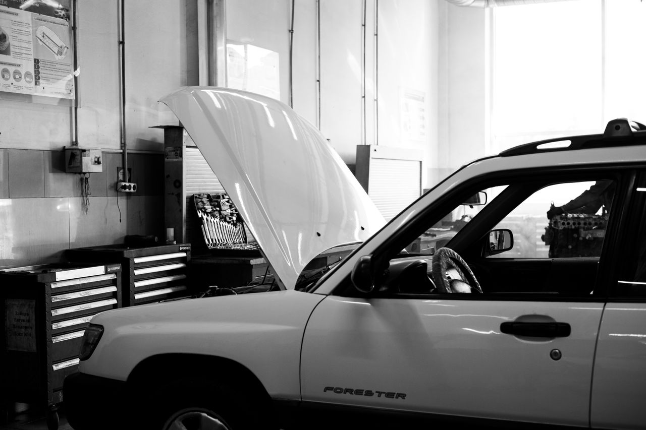 our-mission Black and white photo of a car in an auto repair shop. Hood open for maintenance.